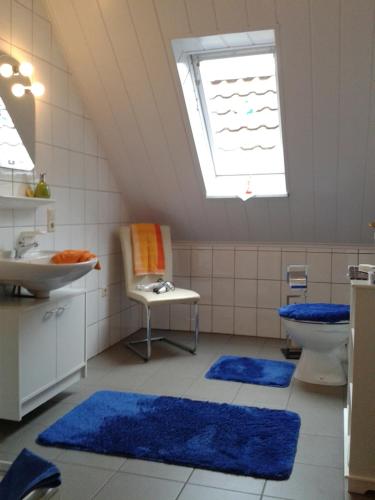 La salle de bains est pourvue de tapis bleus, d'un lavabo et d'une fenêtre. dans l'établissement Ferienwohnung Sandhoege, à Börger