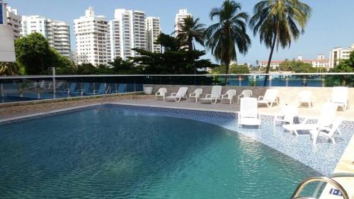 a large swimming pool with white chairs and buildings at Apartamentos Cartagena in Cartagena de Indias