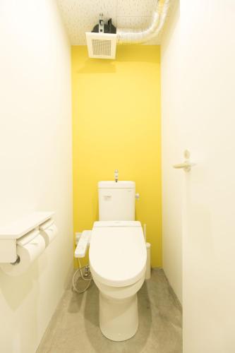a bathroom with a toilet with a yellow wall at hostel DEN in Tokyo