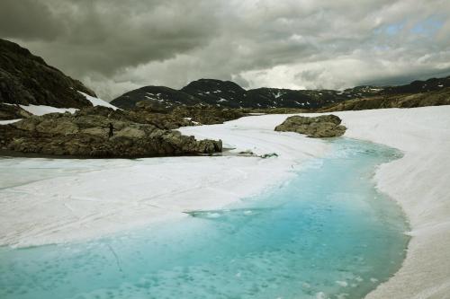a blue pool of water in the snow with mountains at Trolltunga/Folgefonna Camp house in Jondal