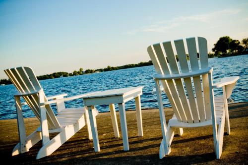 2 chaises et une table sur un quai près de l'eau dans l'établissement The Gananoque Inn & Spa, à Gananoque