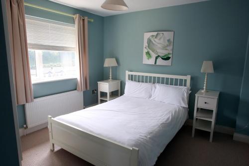 ein blaues Schlafzimmer mit einem weißen Bett und einem Fenster in der Unterkunft Glen Ard Holiday Home No 1 in Dunmore East