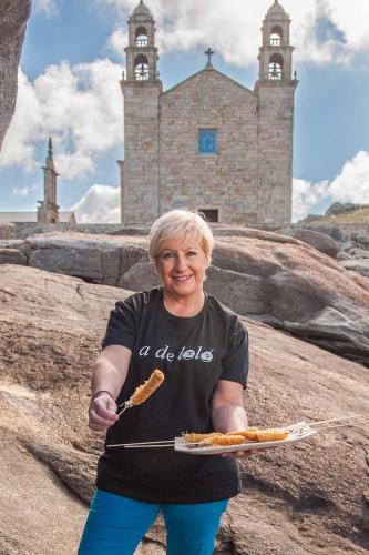 Una mujer sosteniendo un plato de comida frente a una iglesia. en A de Loló Alojamiento con encanto, en Muxía