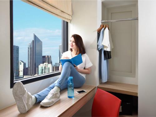 a woman sitting on a window sill reading a book at Hop Inn Hotel Aseana City Manila in Manila
