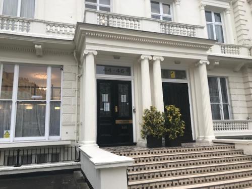 a white house with a black door and stairs at Leinster House (Bayswater) in London
