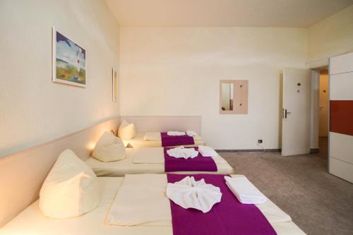 a room with three beds with purple and white sheets at Hotel Margrit in Berlin