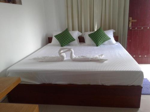 a bedroom with a bed with white sheets and green pillows at Sigiriya Water Guest & View Point Restaurant in Sigiriya