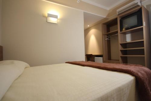 a bedroom with a white bed and a television at Água Viva Hotel in Olímpia