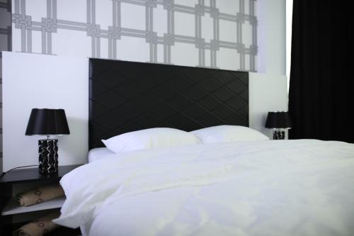 a white bed with a black headboard and two lamps at Hotel Antika in Peje