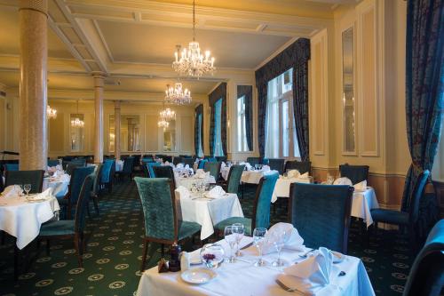 a dining room with white tables and blue chairs at Hydro Hotel in Eastbourne