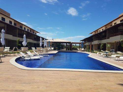 una piscina en un hotel con sillas y sombrillas en Village Beira Mar em Itacimirim, en Itacimirim