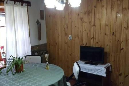 Habitación con mesa, TV y paredes de madera. en Tu Cabaña en San Martín de los Andes