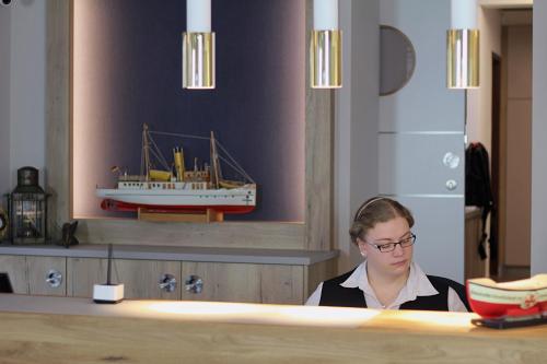 una mujer sentada en un mostrador con un barco en la pared en Hotel Wehrburg, en Cuxhaven