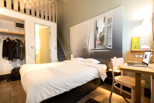 a bedroom with a bed and a desk with a laptop at B&B HOTEL Rennes Nord St Grégoire in Saint-Grégoire