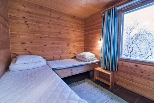 two beds in a wooden room with a window at Saivaara Cottages in Kilpisjärvi