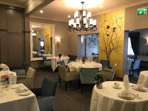 ミルトン・キーンズにあるWoughton House Hotelの白いテーブルと椅子、シャンデリアのあるレストラン