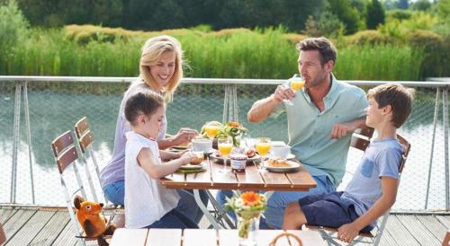 a family sitting at a table eating food on a deck at Ravensburger Spieleland Feriendorf in Meckenbeuren