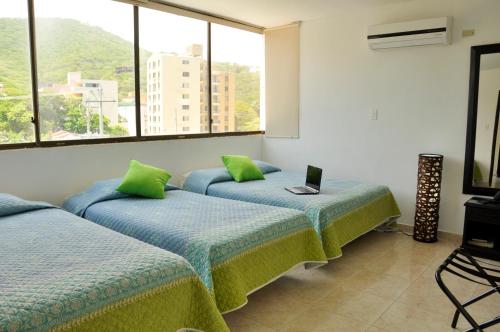 Habitación con 3 camas con almohadas verdes y ventana. en Hotel Yuldama Rodadero Inn, en Santa Marta