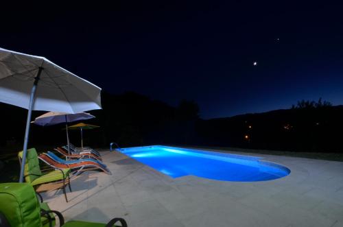 a swimming pool at night with two chairs and an umbrella at Cantinho da Pedra in Vieira do Minho