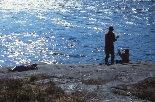a couple of people standing on a rock near the water at Piilijärvi Camping in Gällivare