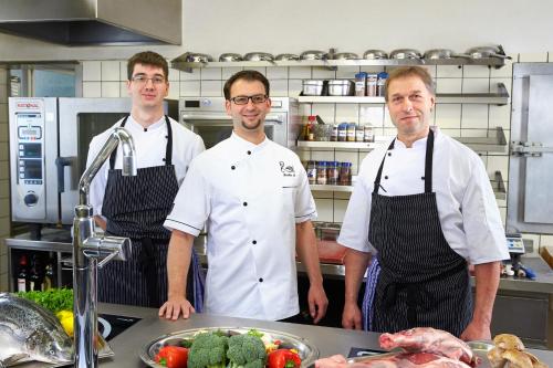 three chefs standing in a kitchen with a table of food at Flair Hotel Schwanen in Bad Bellingen