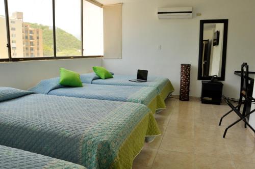 a room with three beds with green pillows at Hotel Axis Inn By GEH Suites in Santa Marta