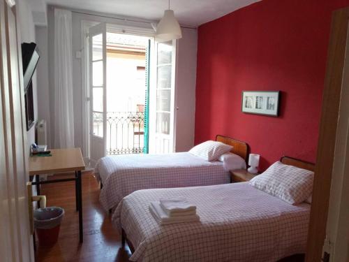 two beds in a room with a red wall at Pensión Manoli in Bilbao