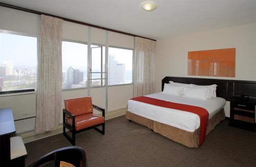 a hotel room with a bed and a chair and windows at Coastlands Durban Self Catering Holiday Apartments in Durban