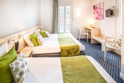 a hotel room with two beds and a desk at H&ocirc;tel Notre Dame de France in Lourdes