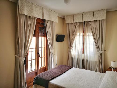 a bedroom with a bed and a window with curtains at Hostal Alcántara in Ávila