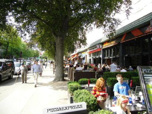 a street with people sitting at tables on a sidewalk at Great Loft & Location by Belsize Park tube in London