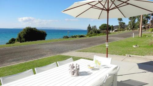 a white table with an umbrella and chairs and the ocean at Millpond. in Penneshaw