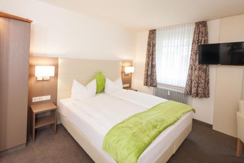 a bedroom with a large white bed with a green blanket at City Hotel Freiburg in Freiburg im Breisgau