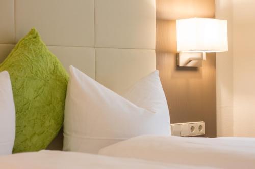 a bed with white pillows and a light on the wall at City Hotel Freiburg in Freiburg im Breisgau