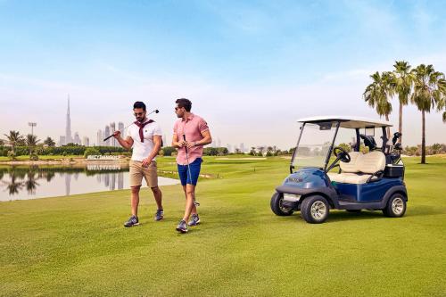 two men standing on a golf course with a golf cart at The Meydan Hotel Dubai in Dubai