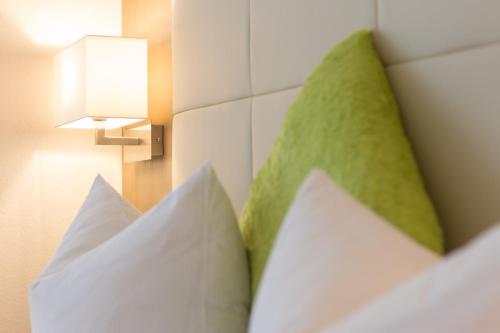 a bed with white pillows and a light on a wall at City Hotel Freiburg in Freiburg im Breisgau