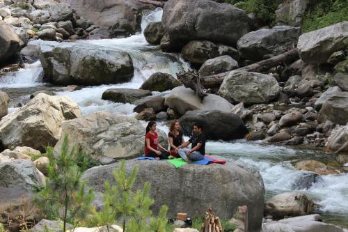 two people sitting on a rock by a river at Tirthan Anglers' Retreat in Banjār