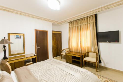 a bedroom with a bed and a desk and a television at Résidence Hôtelière Le Jomonia in Libreville