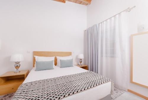 a white bedroom with a bed and two lamps at Pico Dreams in São Roque do Pico