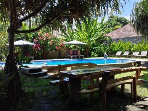 a swimming pool with benches and a picnic table at Suka Sari Cottages in Pemuteran