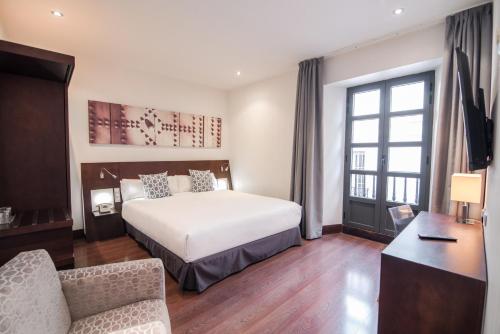 Habitación de hotel con cama, silla y escritorio. en Petit Palace Marques Santa Ana, en Sevilla