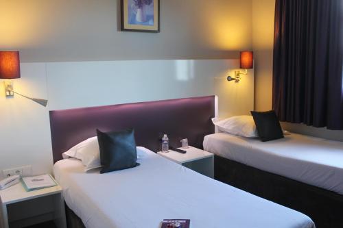 a hotel room with two beds and two tables at The Originals City, Hotel Novella Premium, Nantes Est in Carquefou
