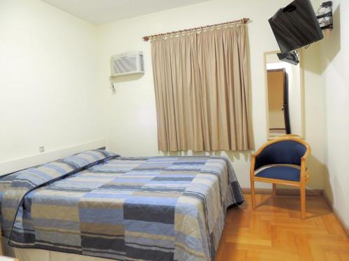 a bedroom with a bed and a chair and a window at Hotel Hetropolis in São Bernardo do Campo