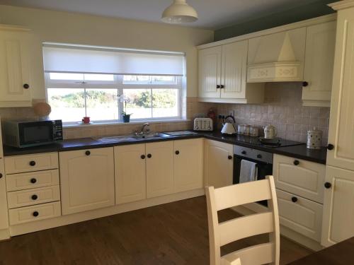 eine Küche mit weißen Schränken, einem Waschbecken und einem Fenster in der Unterkunft No 4 Ballymastoker Cottage in Portsalon
