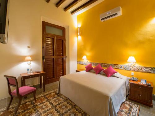 a bedroom with a bed and a table and a chair at Hotel del Gobernador in Mérida