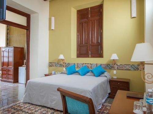 a bedroom with a large bed with blue pillows at Hotel del Gobernador in Mérida