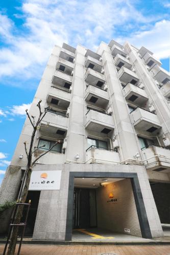 a tall white building with a tree in front of it at Hotel Yumeya in Fukuoka
