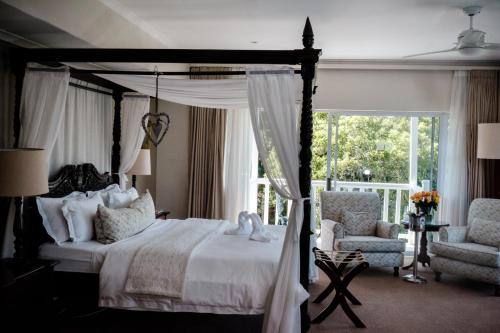 a bedroom with a canopy bed and two chairs at Cinnamon Boutique Guest House in Wilderness