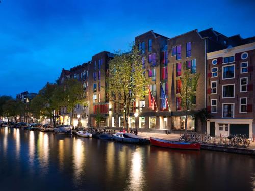 einen Fluss mit Booten in einer Stadt in der Nacht in der Unterkunft Andaz Amsterdam Prinsengracht - a concept by Hyatt in Amsterdam