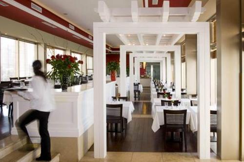 a woman walking through a restaurant with tables and chairs at Leonardo City Tower Hotel Tel Aviv in Tel Aviv